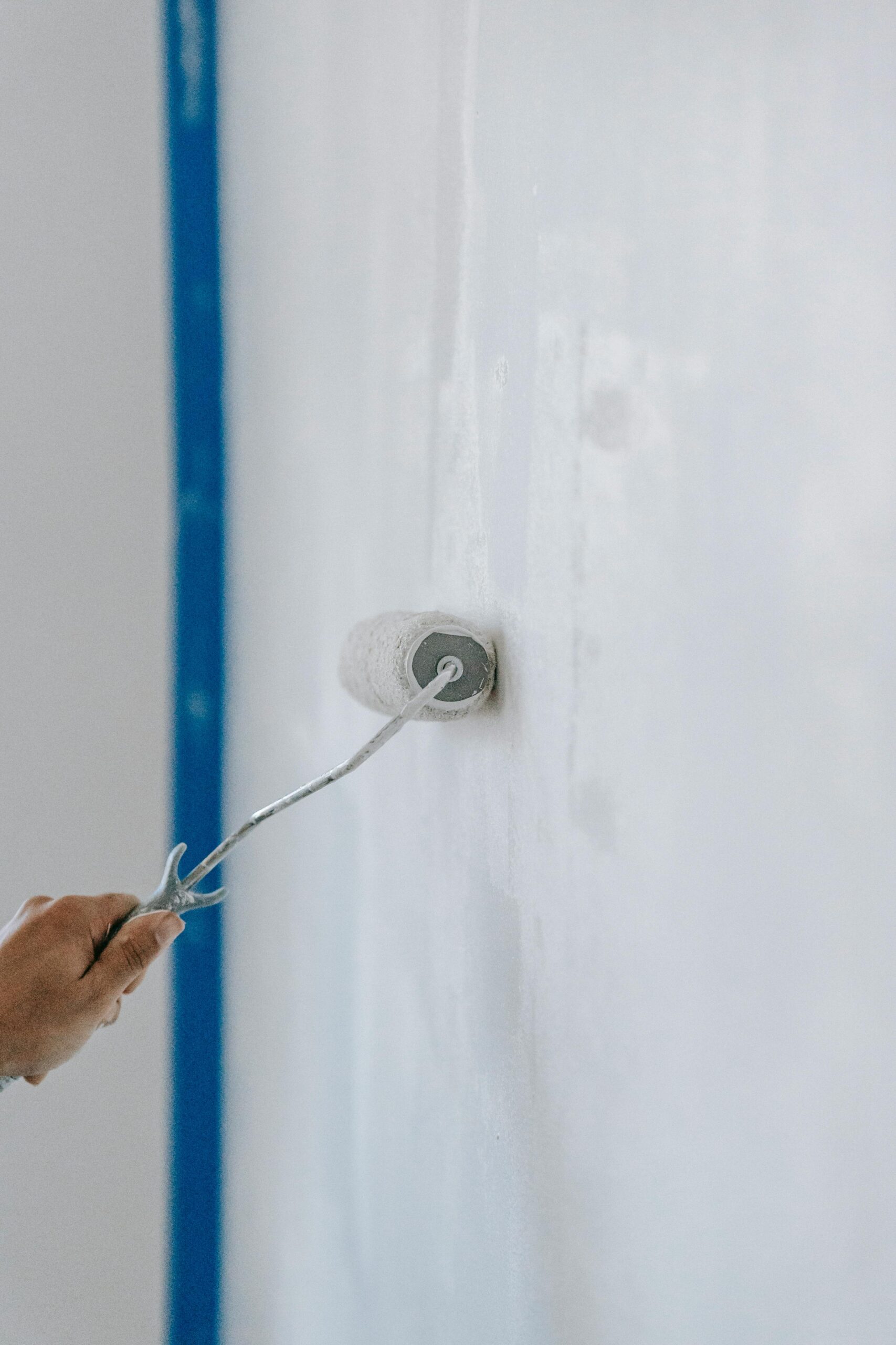 A close-up of a person using a paint roller to apply white paint on an indoor wall.