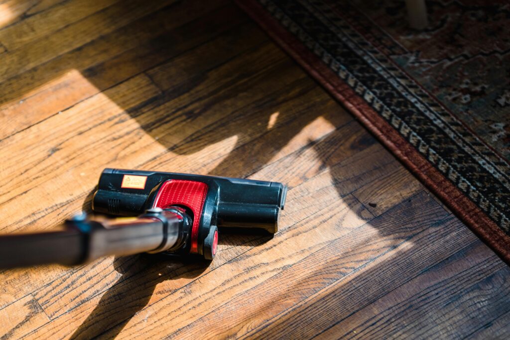 Close-up of a vacuum cleaner on wooden flooring near a patterned rug, showcasing domestic cleaning.